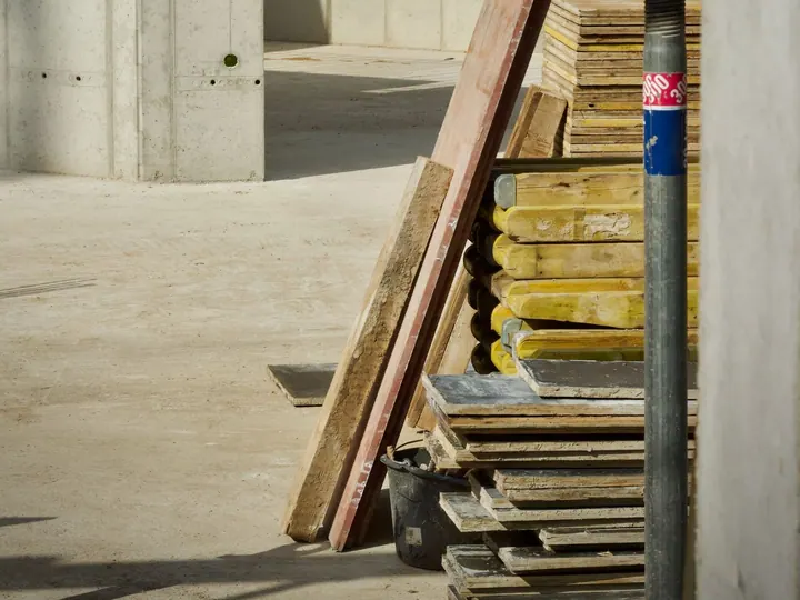 Stacked timber panels beside a concrete wall at a construction site